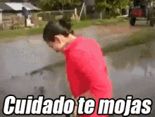 a woman in a red shirt is standing in a puddle with the words cuidado te mojas written above her