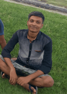 a man in a black shirt sits on the grass with his legs crossed