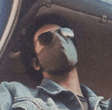 a man wearing sunglasses and a mask looks out the window of a car