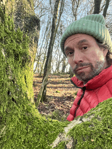 a man wearing a green hat and a red jacket is standing next to a tree