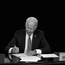 a black and white photo of a man sitting at a desk with the words under biden the deficit written on the bottom