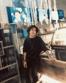 a man leans on a counter in front of a display case that says mad ayush cafe