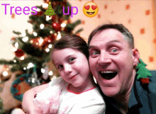 a man and a little girl are posing in front of a christmas tree with the words trees up on the bottom