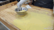 a person is mixing something in a metal bowl on a wooden table with the words made in animotica on the bottom