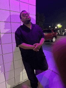 a man leaning against a wall with a purple light behind him