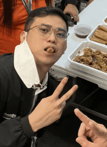 a man wearing glasses and a mask is eating a piece of food and giving a peace sign