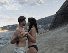 a shirtless man and a woman in a bikini are holding hands on a beach