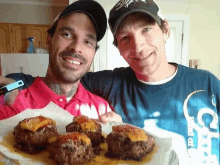 two men standing next to each other holding a plate of meatballs with cheese on top