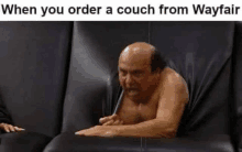 a bald man is laying on a black couch with a pen in his mouth .