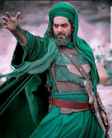 a man with a beard and a green cape holds a sword in his right hand