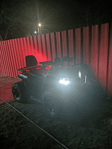 a black atv is parked in front of a red fence at night