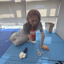 a woman sitting on the floor drinking from a red cup with a straw