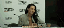 a woman is sitting at a table with a microphone in front of a wall that says fan expo .