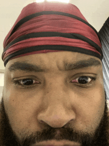 a man with a beard wearing a red and black headband looks at the camera