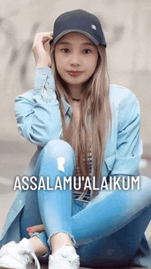 a woman wearing a blue jacket and a black hat sits on the ground with the words assalamu ' alaikum above her