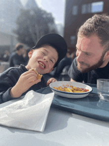 a man and a child are sitting at a table with a plate of food in front of them