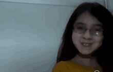 a young girl wearing glasses and a yellow shirt is smiling and looking at the camera .