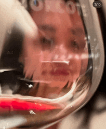 a woman 's face is reflected in a glass of wine with the number 2/10 on the bottom