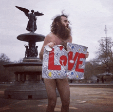 a naked man is holding a sign that says love in front of a fountain