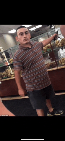 a man in a striped shirt and shorts is standing in front of a bakery display .