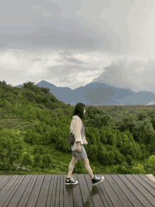 a woman is walking on a wooden deck overlooking a forest