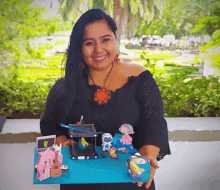 a woman in a black top is holding a blue board with toys on it and smiling