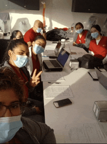 a group of people wearing face masks are sitting at a table with laptops