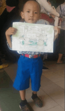 a young boy in blue shorts holds up a drawing