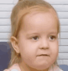 a little girl with blonde hair is making a funny face .