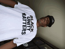 a man wearing a black hat and a white t-shirt that says black unity matters