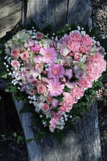 a heart shaped bouquet of pink and white flowers is sitting on top of a wooden table .