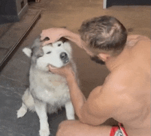 a shirtless man is petting a husky dog 's face .