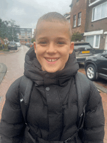 a young boy wearing a black jacket and a backpack is smiling for the camera