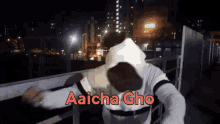 a man in a white hoodie is standing on a balcony with the words aaicha gho above him