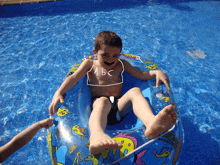 a boy with a fake mustache is floating in a swimming pool with abc written on his chest