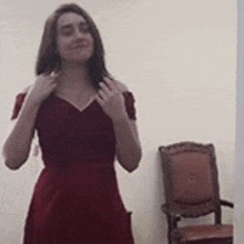 a woman in a red dress is standing in front of a chair in a room .