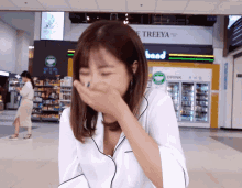 a woman covering her mouth with her hand in front of a store that has the word drink on it