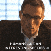 a man wearing glasses and a suit is sitting in a chair and says humans are an interesting species .