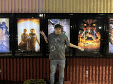 a man stands in front of a row of movie posters including one for star wars episode 1