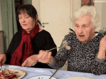 two elderly women are sitting at a table with plates of food and spoons in their hands with the hashtag trendizisst visible