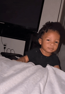 a little girl laying on a bed with a tv in the background