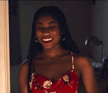 a woman wearing a red floral dress and hoop earrings smiles