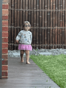 a little girl wearing heart shaped sunglasses is walking barefoot on a wooden deck