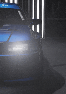 a blue car is parked in a dark room with a white light behind it