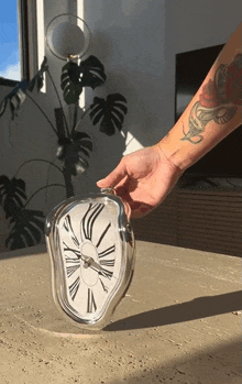 a person with a tattoo on their arm is pointing at a clock on a table