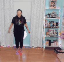 a woman wearing a black shirt with a dragon on it is standing in front of a shelf full of toys