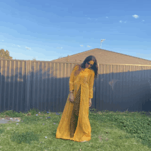 a woman in a long yellow dress is standing in front of a fence