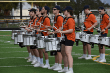 a marching band is playing their drums on a field and they are wearing orange shirts with the word falcons on them