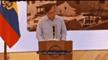 a man stands at a podium with a flag behind him and the words @vallenatopabeber on the bottom