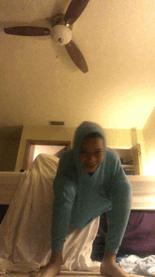 a person wearing a blue sweatshirt is crawling under a ceiling fan